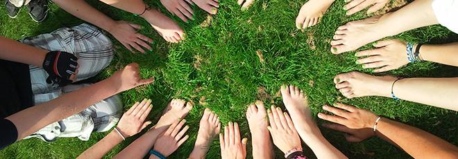 A bunch of people's hands and feet in a circle on green grass